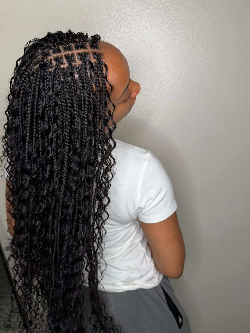 Long bohemian knotless box braids with loose curly ends and clean square partings, shown in side profile against a white wall