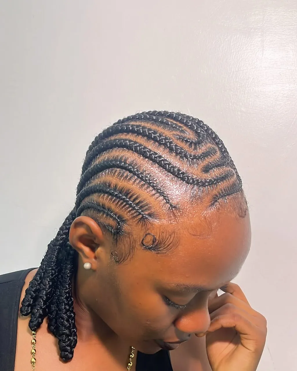 Feed-in stitch cornrows braided straight back and gathered into a side ponytail of braids draped over one shoulder, with laid edges