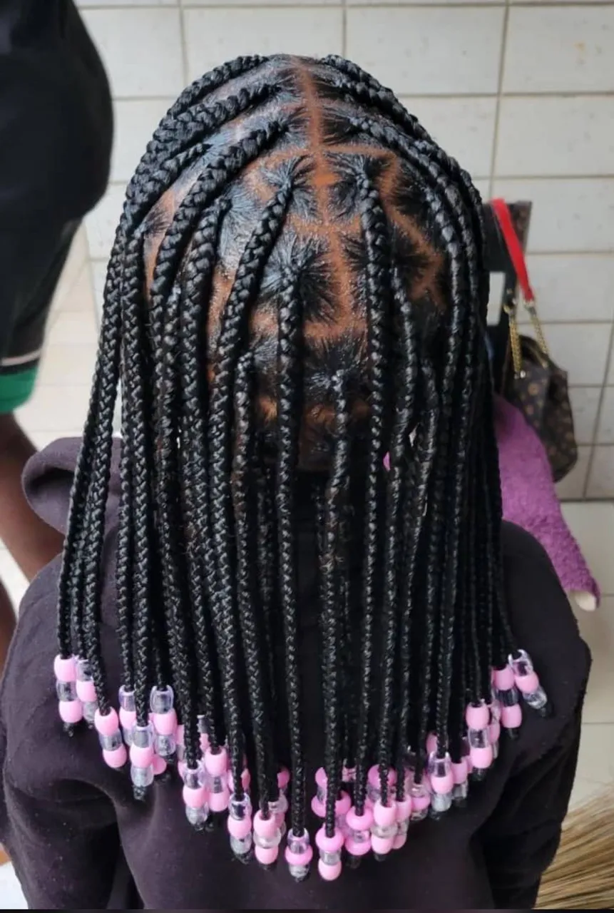 Child's knotless box braids in a clean grid part, ending in shoulder-length braids finished with pink and clear beads