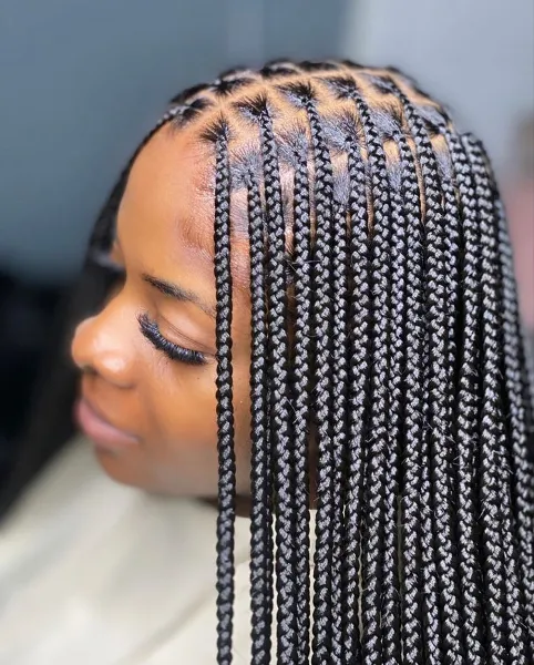 Long sleek knotless box braids with neat triangle parts at the crown, swept forward over one shoulder in a soft side profile