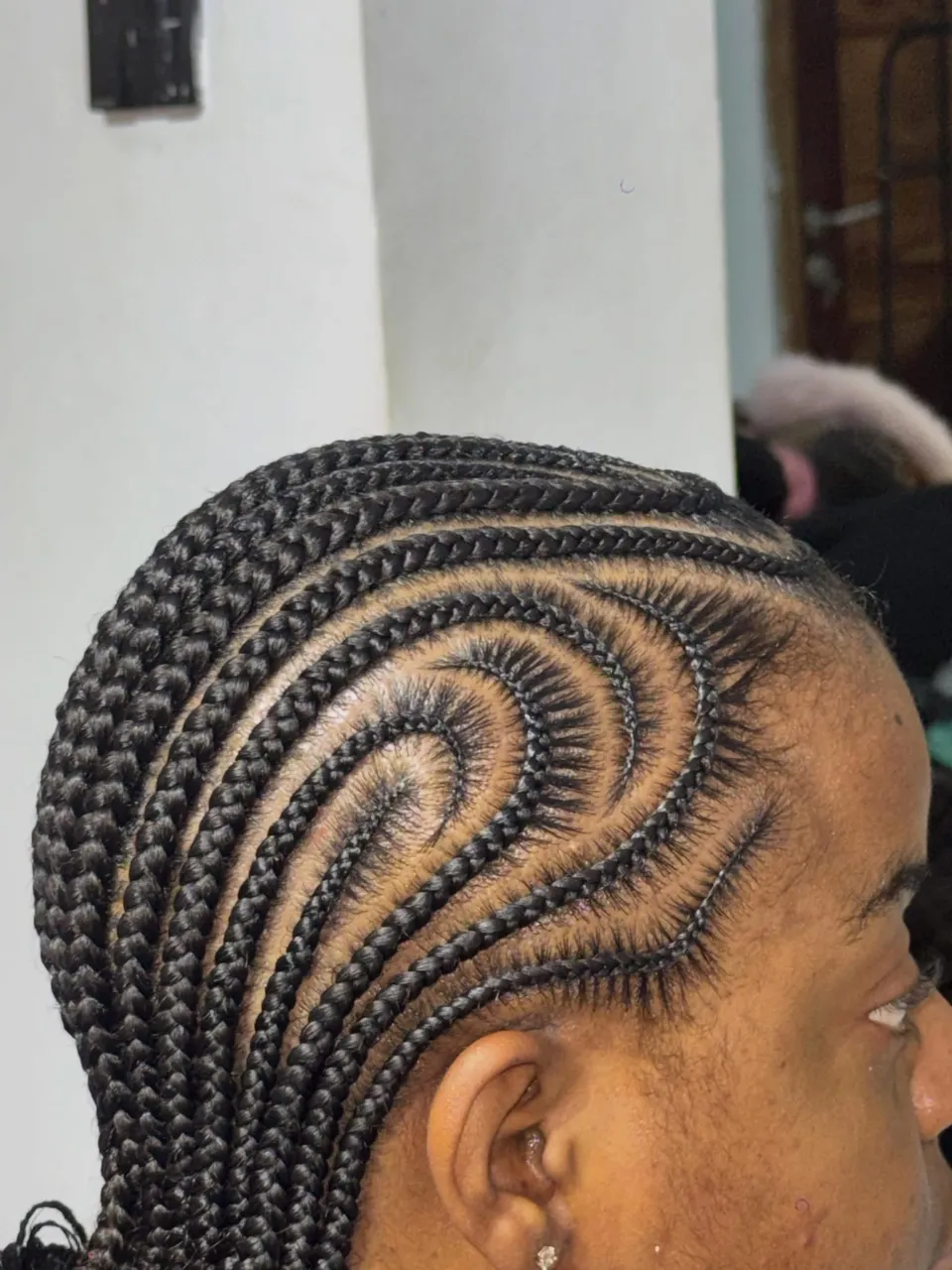 Freestyle feed-in cornrows curving into a central spiral swirl on the crown, with neat clean braid lines